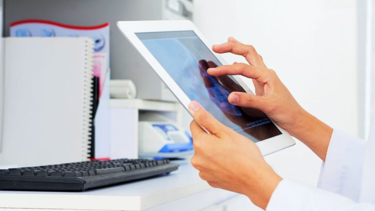 A dental professional analyzing a digital dental X-ray on a tablet in a clinical setting