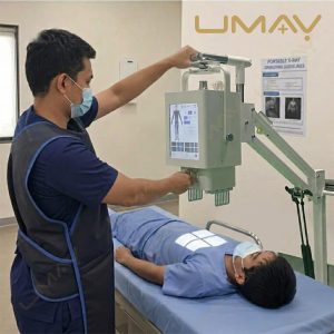 A medical professional wearing a protective lead apron adjusts a portable X-ray machine over a patient lying on an examination table.