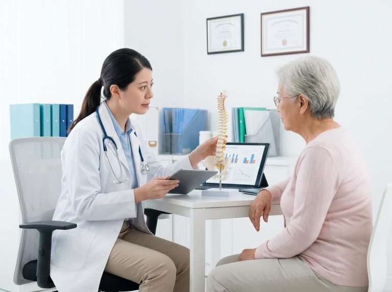 Doctor using spine model to explain osteoporosis treatment to senior patient.