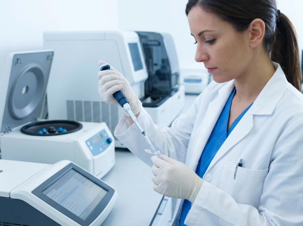 Researcher preparing sample with micropipette near benchtop laboratory centrifuge.
