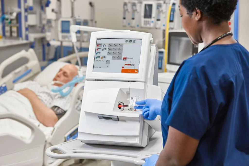 Nurse injecting a blood sample syringe into a point-of-care blood gas and electrolyte analyzer in an ICU.